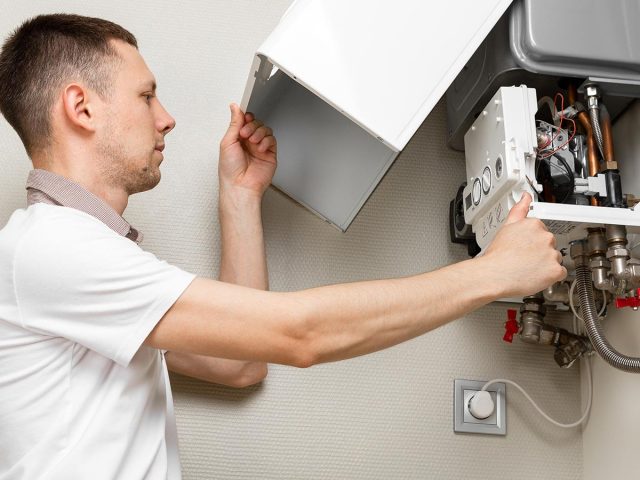 Plumber attaches Trying To Fix the Problem with the Residential Heating Equipment. Repair of a gas boiler